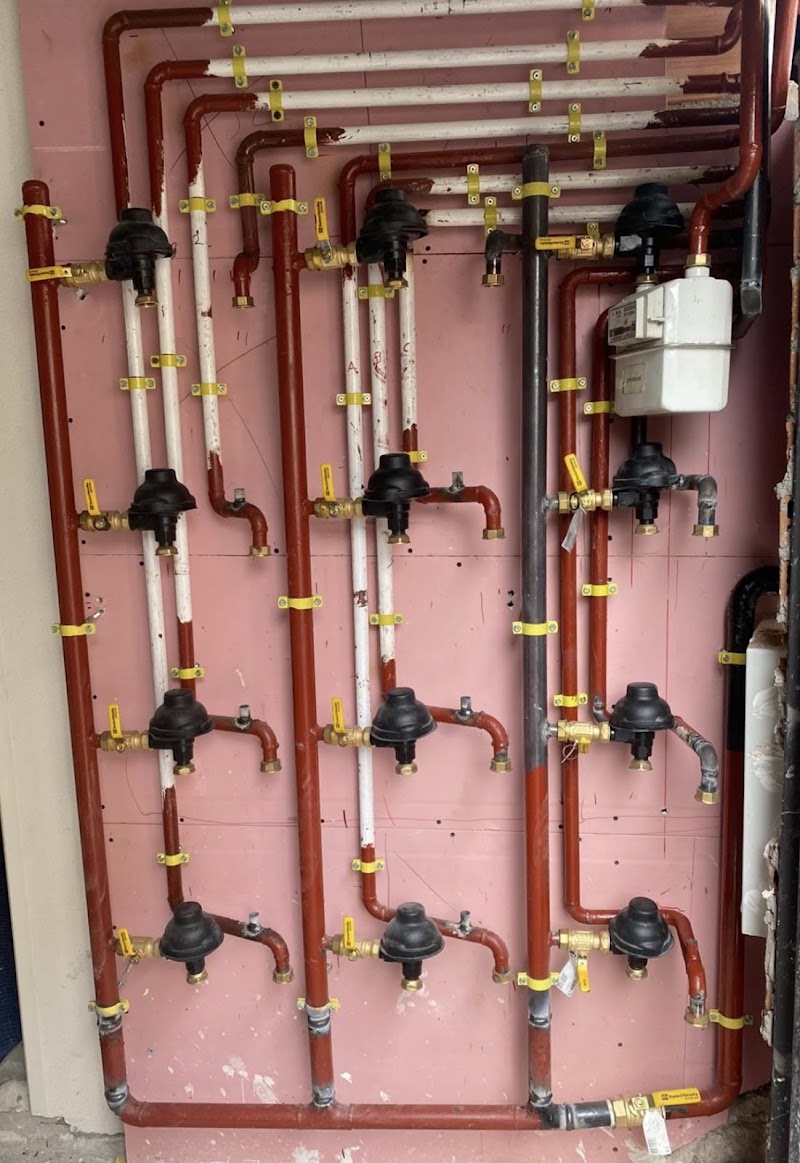 Batería de gas de una comunidad recién montada sobre pared rosa: doce reguladores negros en tres columnas, tubería roja y blanca y un contador arriba a la derecha.